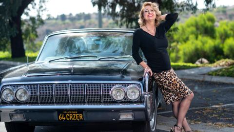 Author posing in front of classic car in black sweater and leopard print skirt