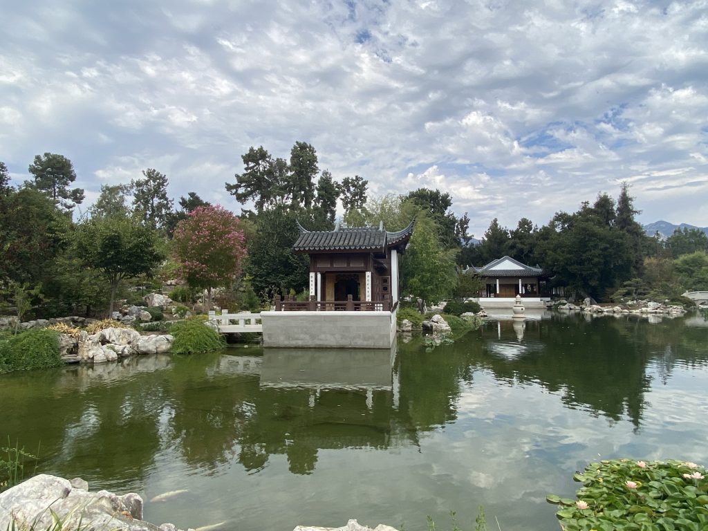In this scene: the Waveless Boat pavilion is in the middle ground, lily pads and stone in the foreground, and the San Gabriel Mountains and trees form the background. (KimberlyUs)